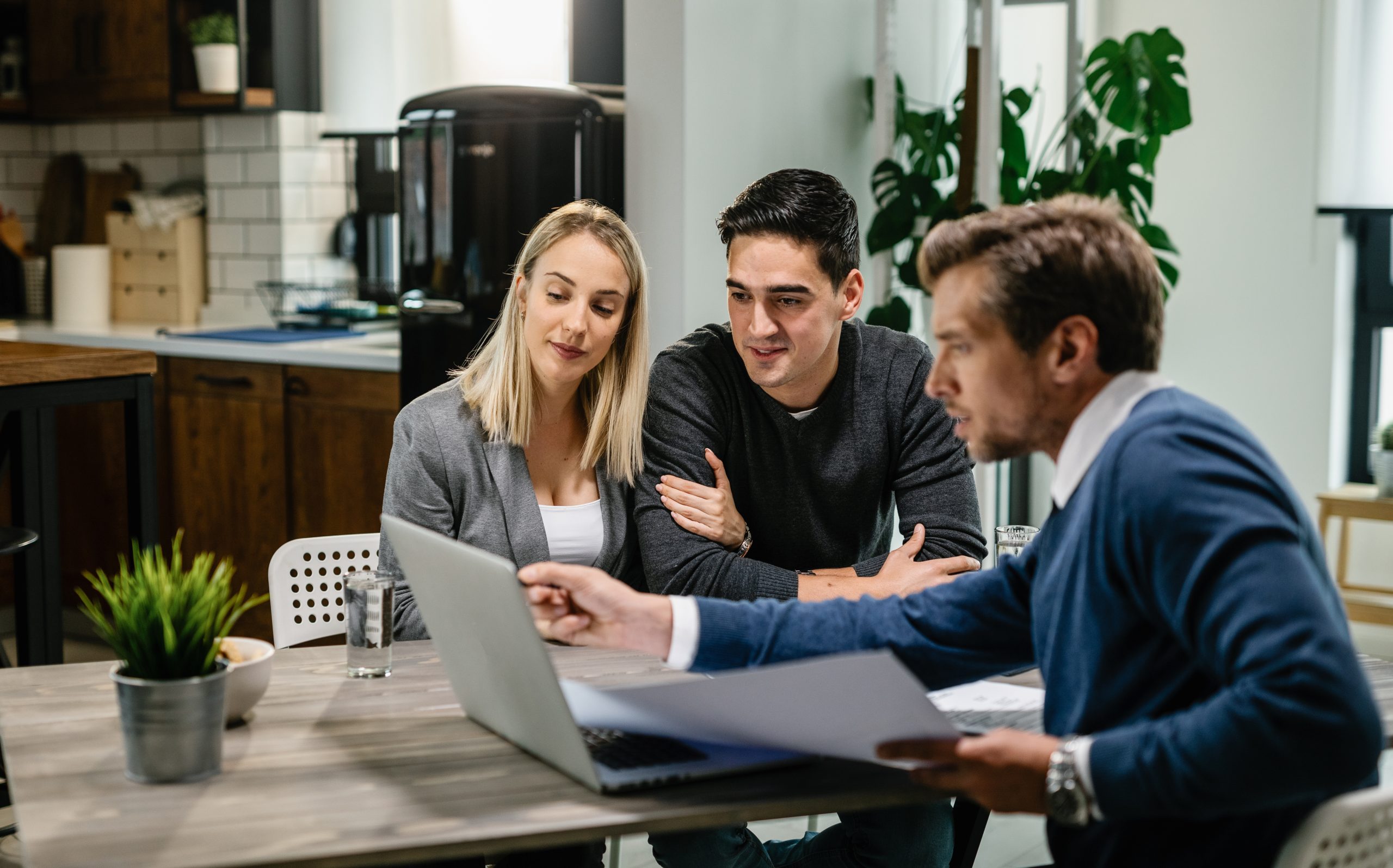 Young couple and real estate agent using laptop while going through housing plan on a meeting.